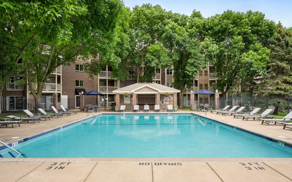 a resort style pool with lounge chairs and a building in the background at Cityscape, St Louis Park, 55416