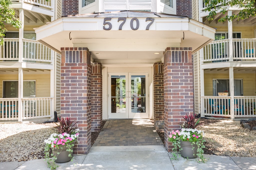 the front entrance of a condo building with flowers on the sidewalk at Cityscape, St Louis Park, MN