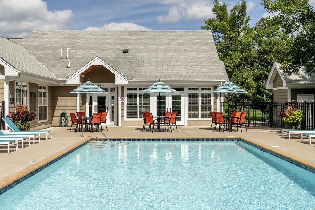 a swimming pool in front of a house with chairs and umbrellas
