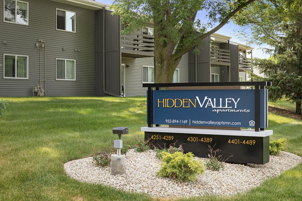 a sign for hiden valley apartments in front of a lawn and a tree