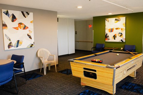 A pool table is in the middle of a room with chairs and artwork on the walls.