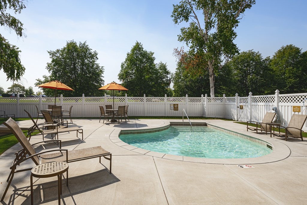 a swimming pool with chairs and umbrellas in a backyard with a white fence