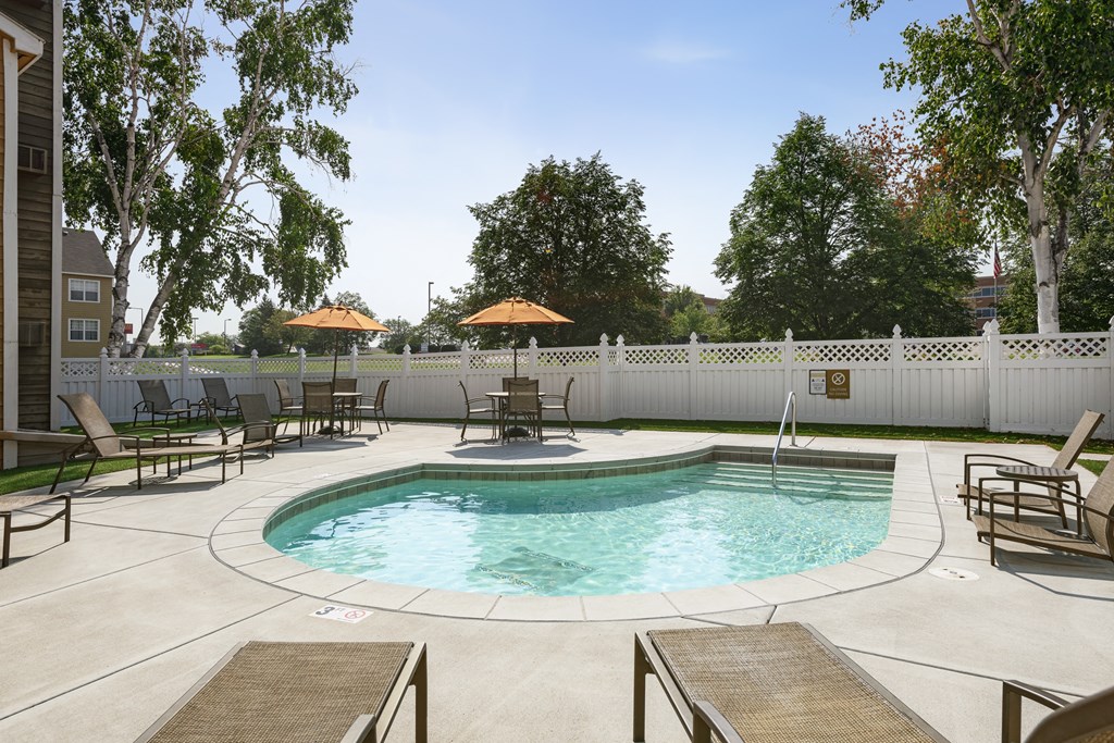 a swimming pool with chairs and umbrellas in a backyard with a white fence