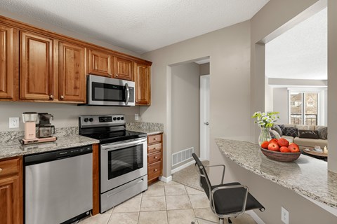 A kitchen with a black fridge and stove, a microwave above it, and a black chair in front of the counter.
