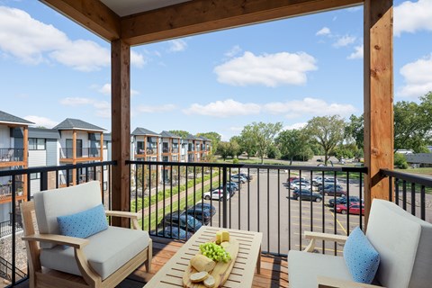 A balcony with chairs and a table with a bowl of fruit on it.