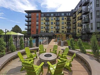 A patio with green chairs and a fire pit in front of apartment buildings.