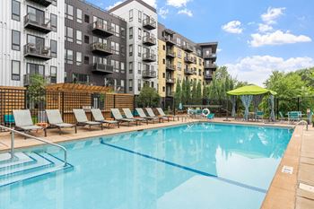 A large swimming pool with lounge chairs and umbrellas in front of apartment buildings.