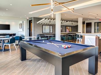A pool table is in the middle of a room with a bar and a TV.