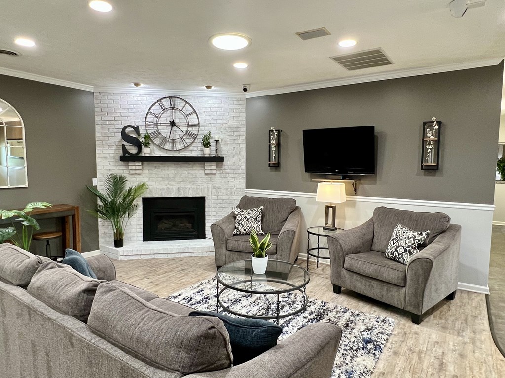 A living room with a grey couch, a fireplace, and a clock on the wall.