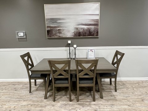 A wooden dining table with four chairs and a painting on the wall.