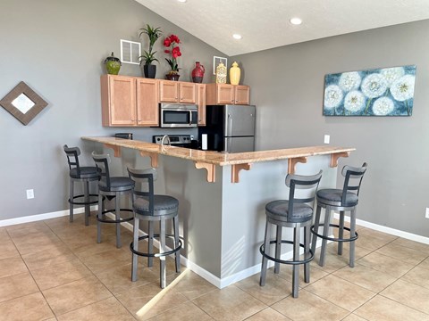 a bar with four stools and a kitchen with a refrigerator and microwave
