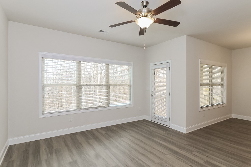 an empty living room with a ceiling fan and windows