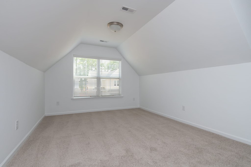 a spacious attic room with white walls and a window