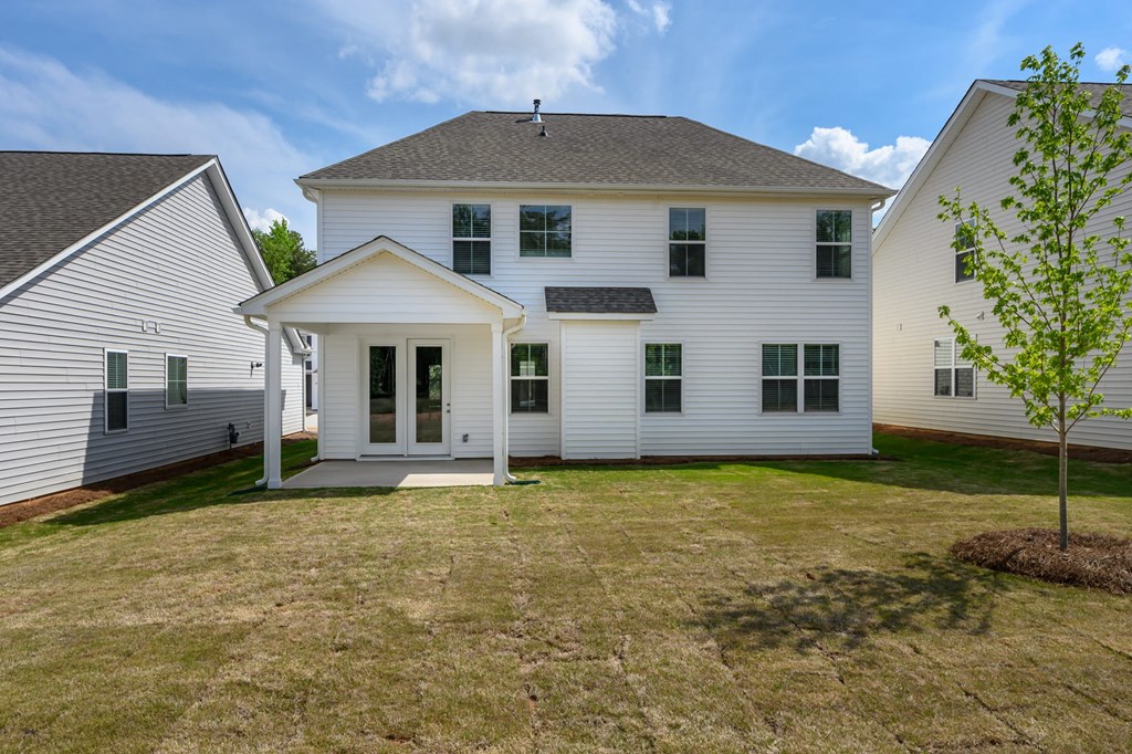the back of a white house with a lawn and a tree