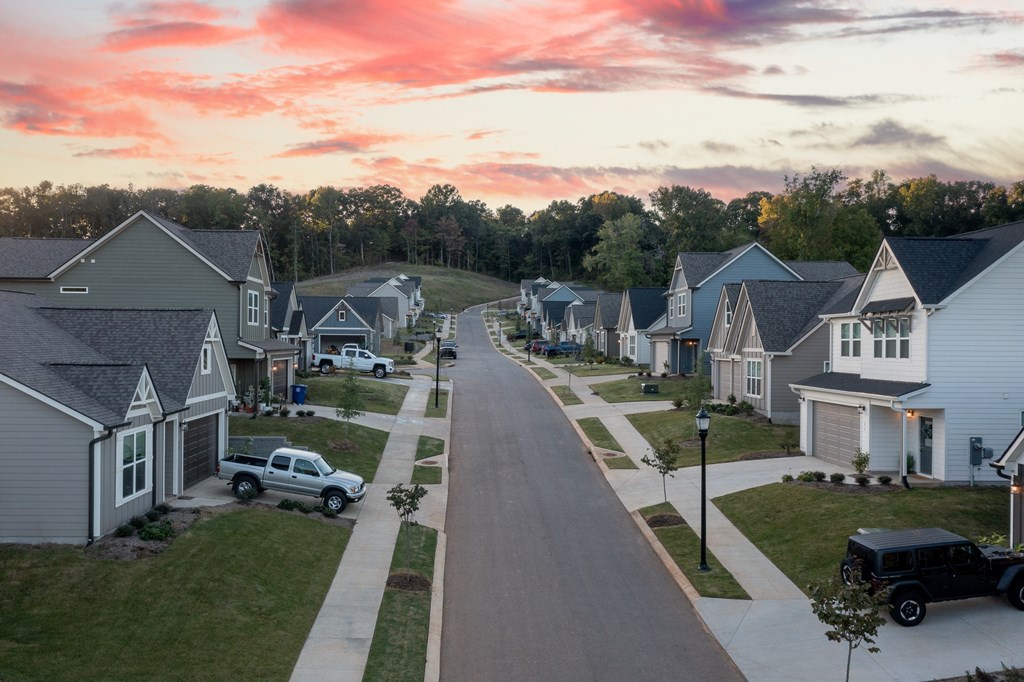A residential street with houses on both sides and cars parked on the right.