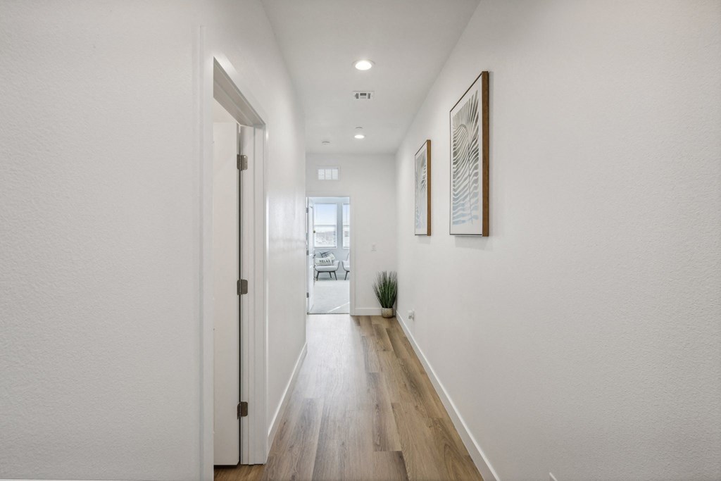 A long hallway with a door on the left and two pictures on the wall.