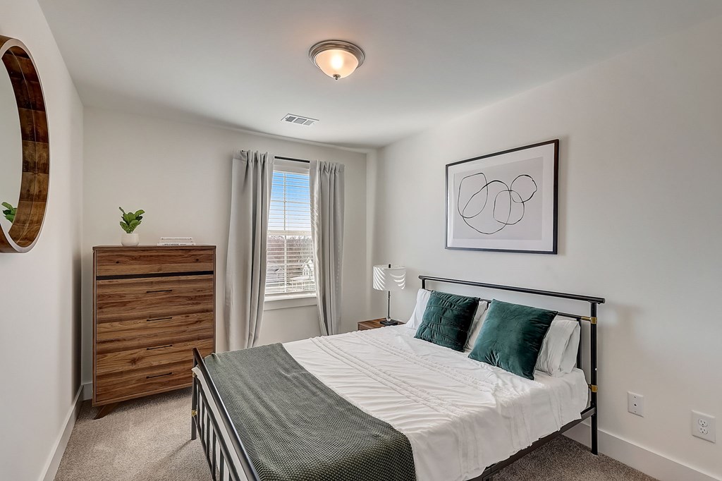 A bedroom with a bed, nightstand, and a plant.