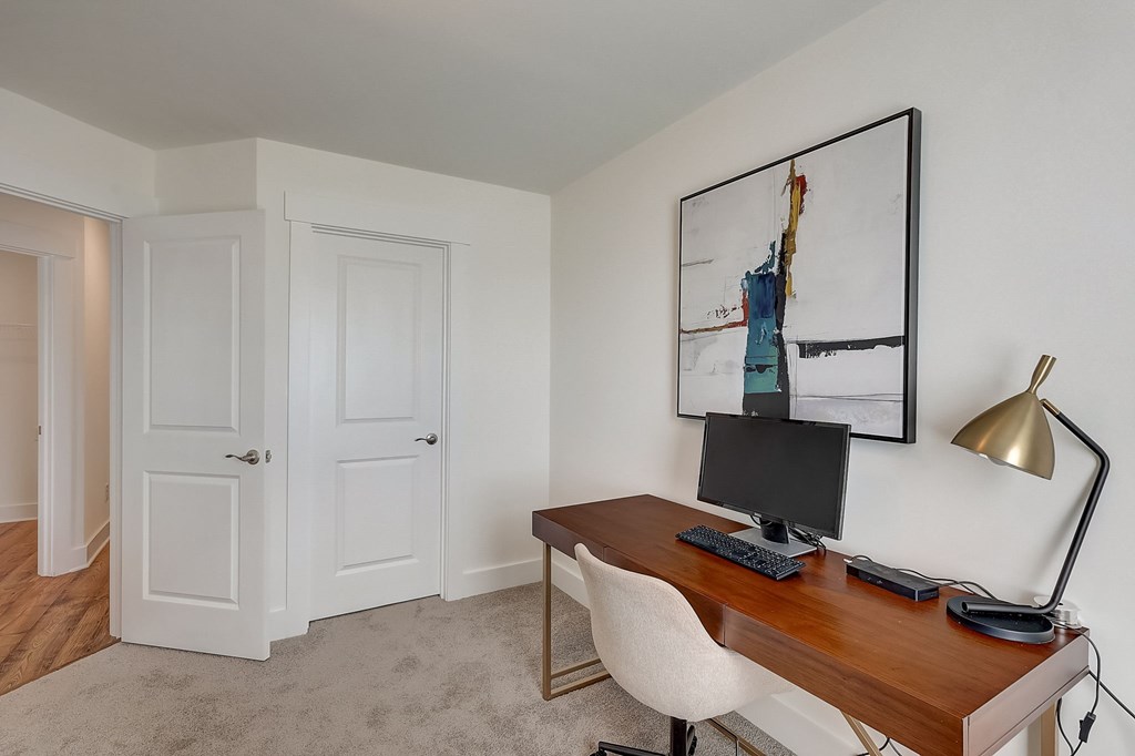 A room with a desk and a chair with a painting hanging on the wall.