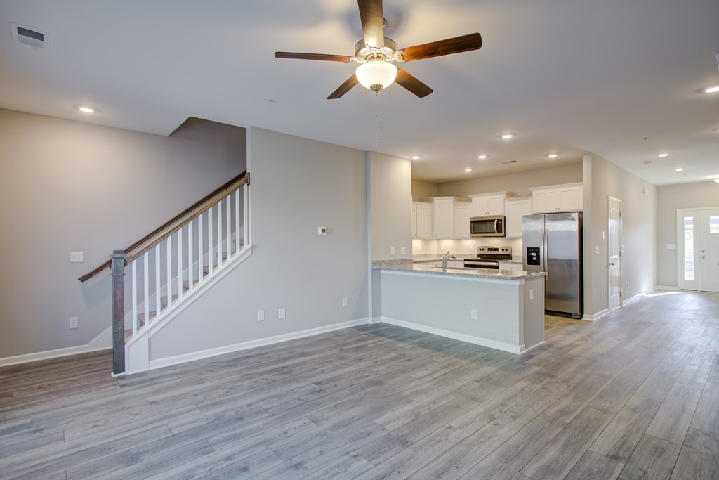 A spacious living room with a staircase and a kitchen in the background.