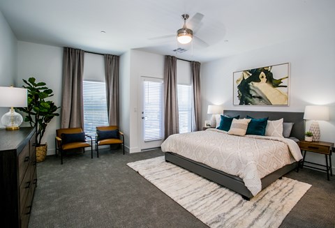 A bedroom with a large bed, a ceiling fan, and a painting on the wall.