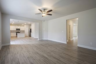 an empty living room with a ceiling fan and a kitchen