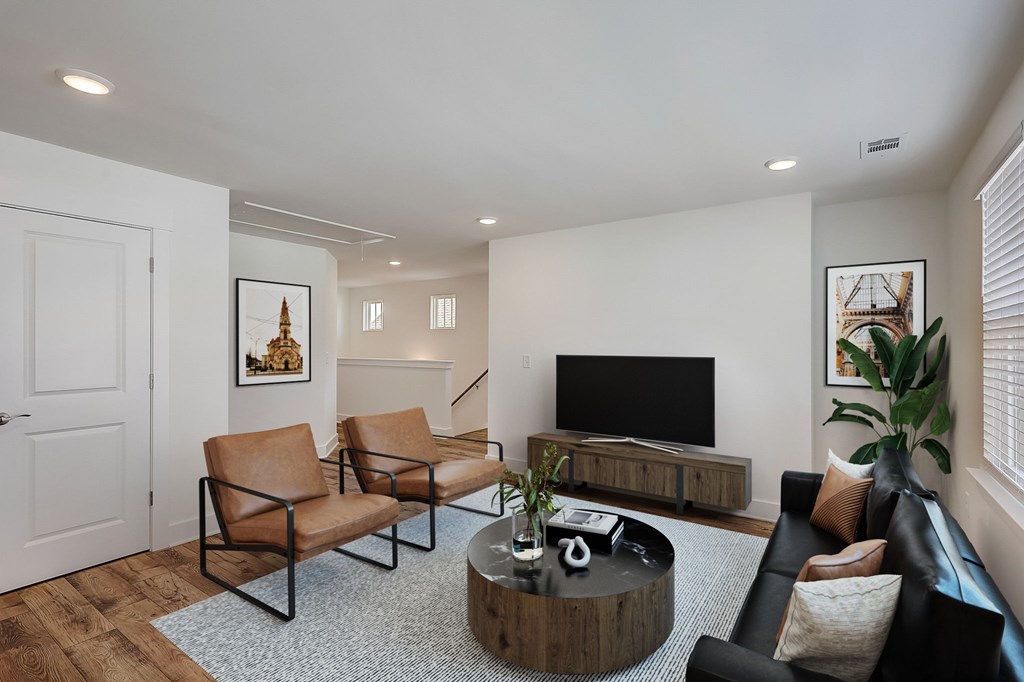 A living room with a black leather couch, a wooden coffee table, and a flat screen TV.