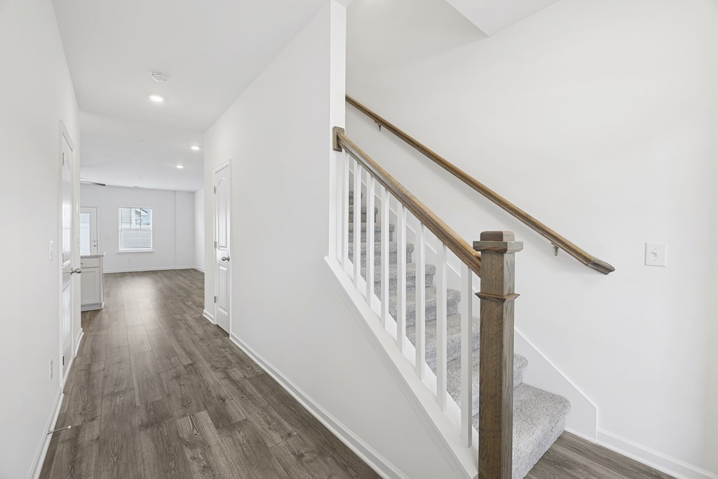 A long hallway with a staircase and wood flooring.