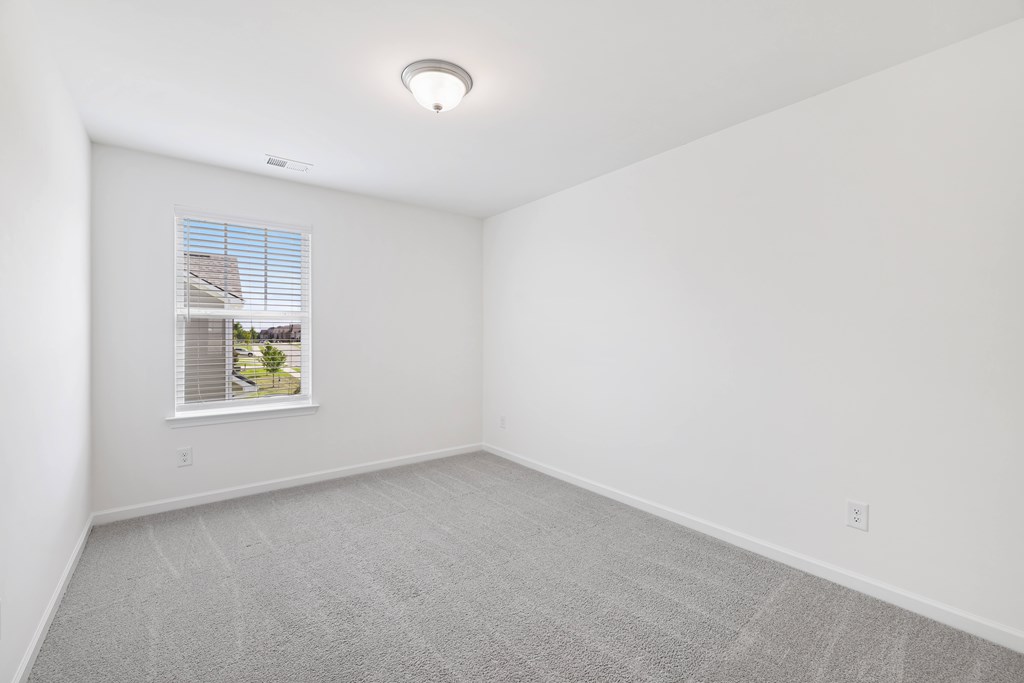 A room with a window and a grey carpet.