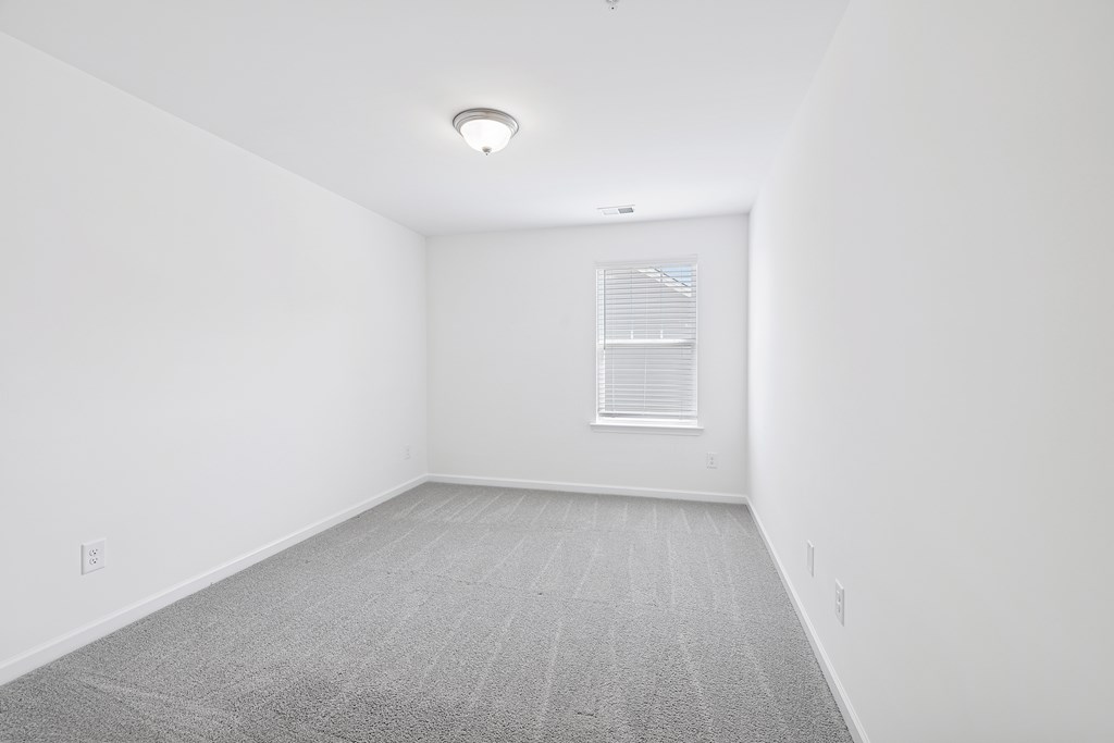 A room with a carpeted floor and a window with blinds.