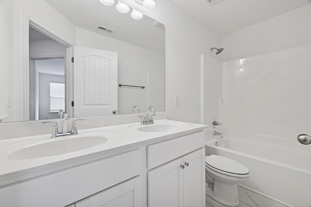 A white bathroom with a double sink and a toilet.