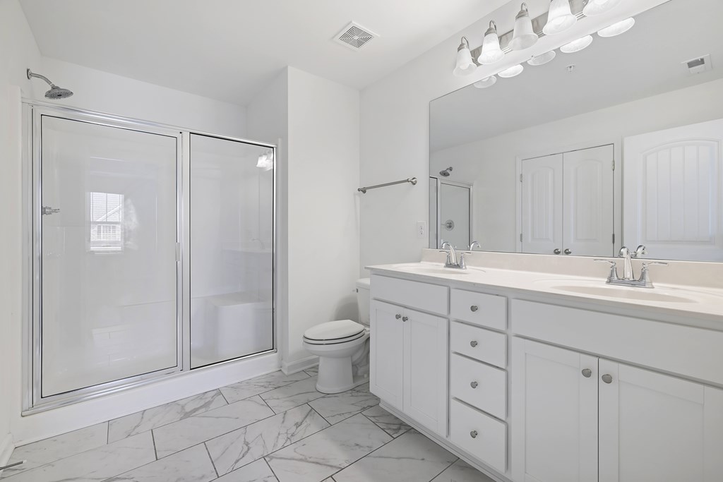 A white bathroom with a marble floor and a large mirror.