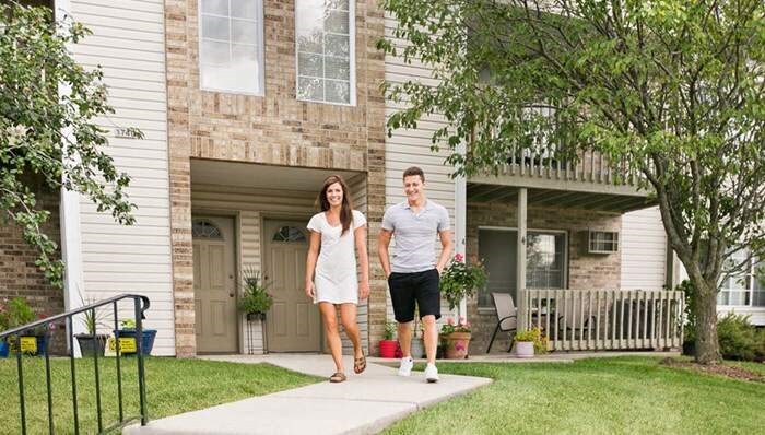 a man and woman walking down the sidewalk in front of a house