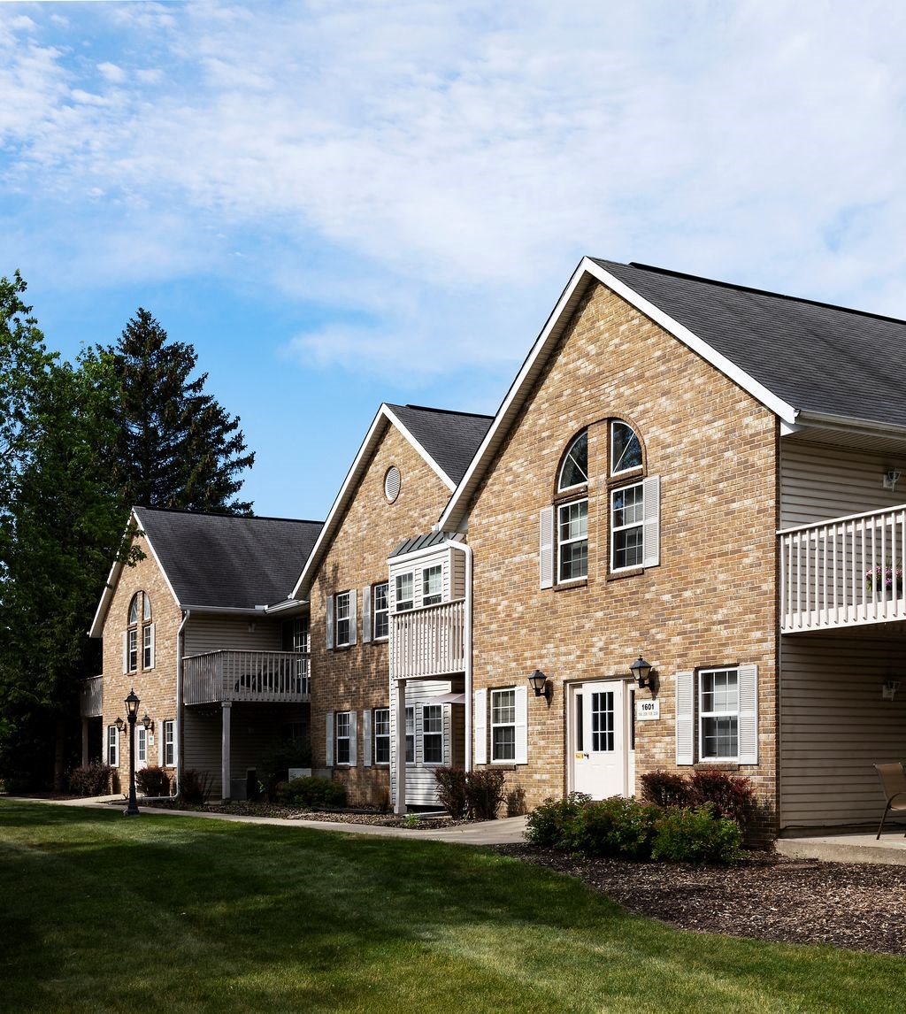 the front of a brick house with a porch and a lawn