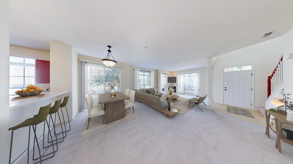 A well-lit, spacious living room with a dining area and a kitchen in the background.