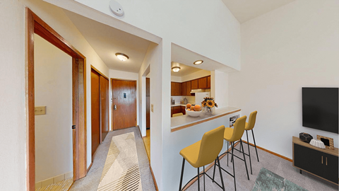 A hallway with a striped carpet leads to a kitchen area with a bar and chairs.