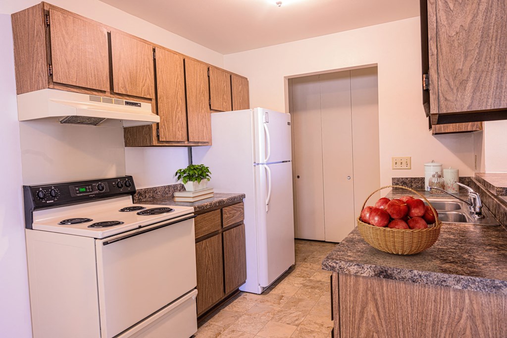 a kitchen with white appliances and wooden cabinets and a basket of apples