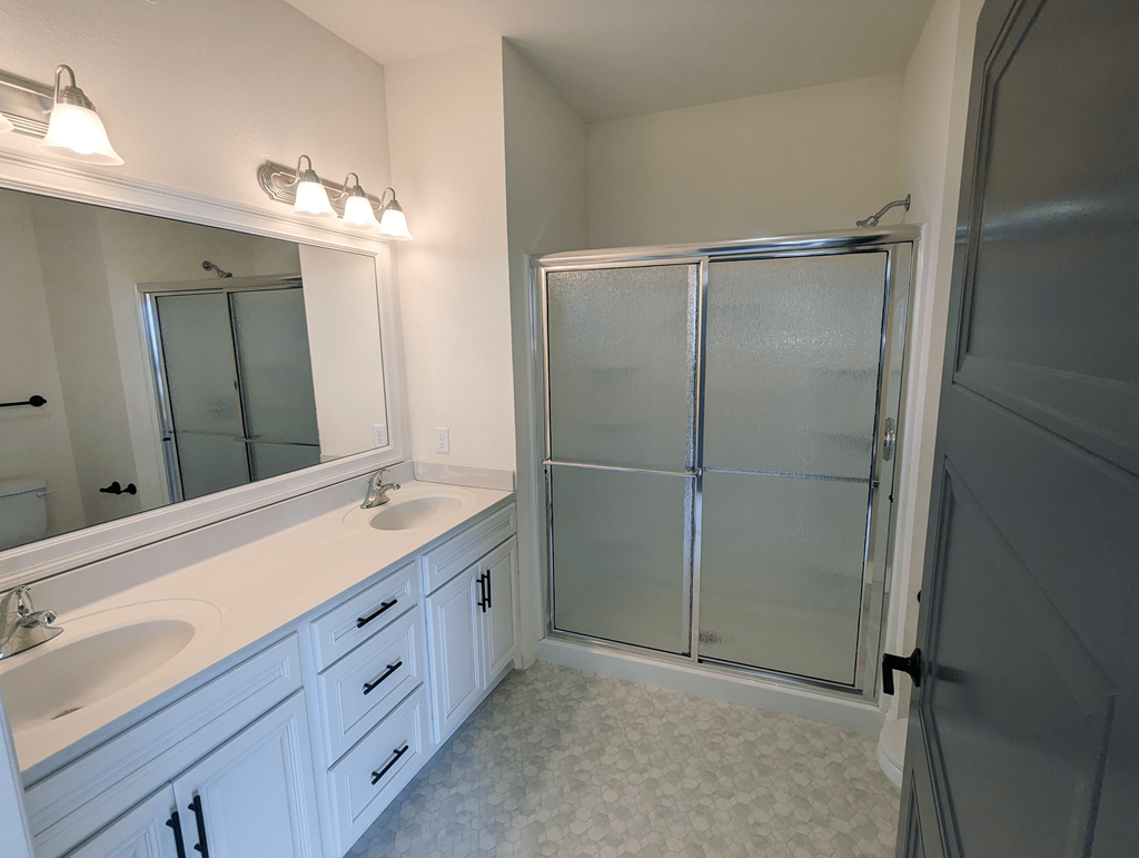 a bathroom with white cabinets and a shower and sink