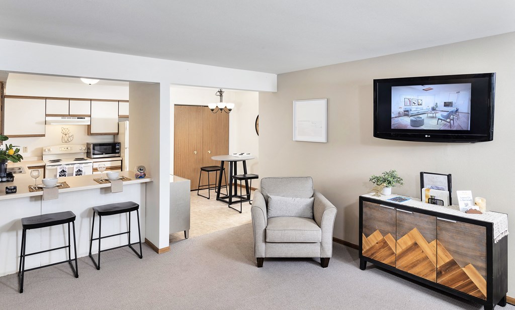 a living room with a tv and a kitchen with a bar and stools