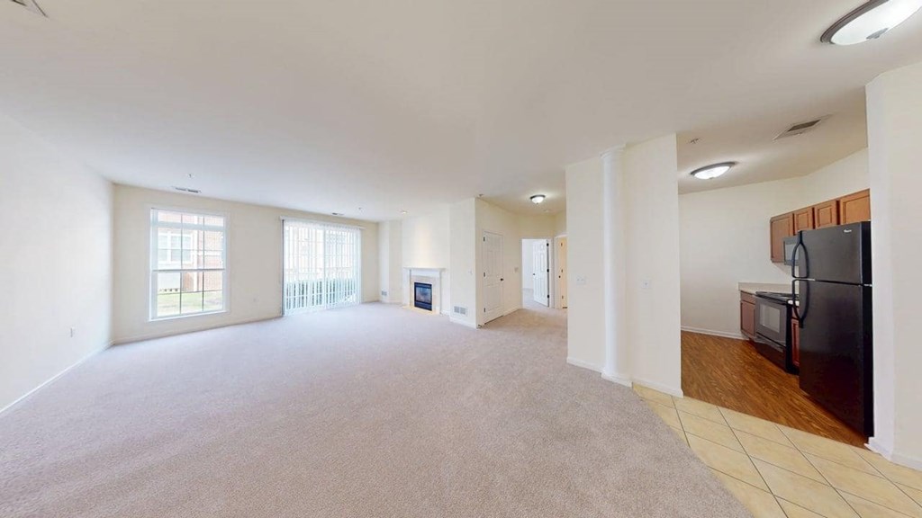 A spacious living room with a grey carpet and a black refrigerator.