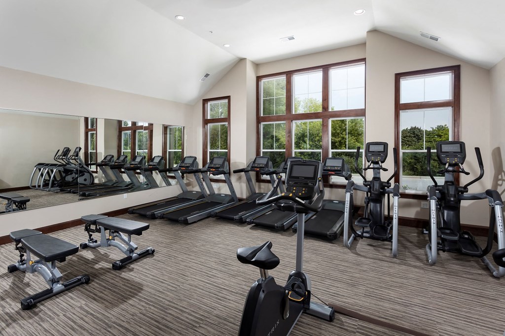 a gym with cardio equipment and weights in a building with windows