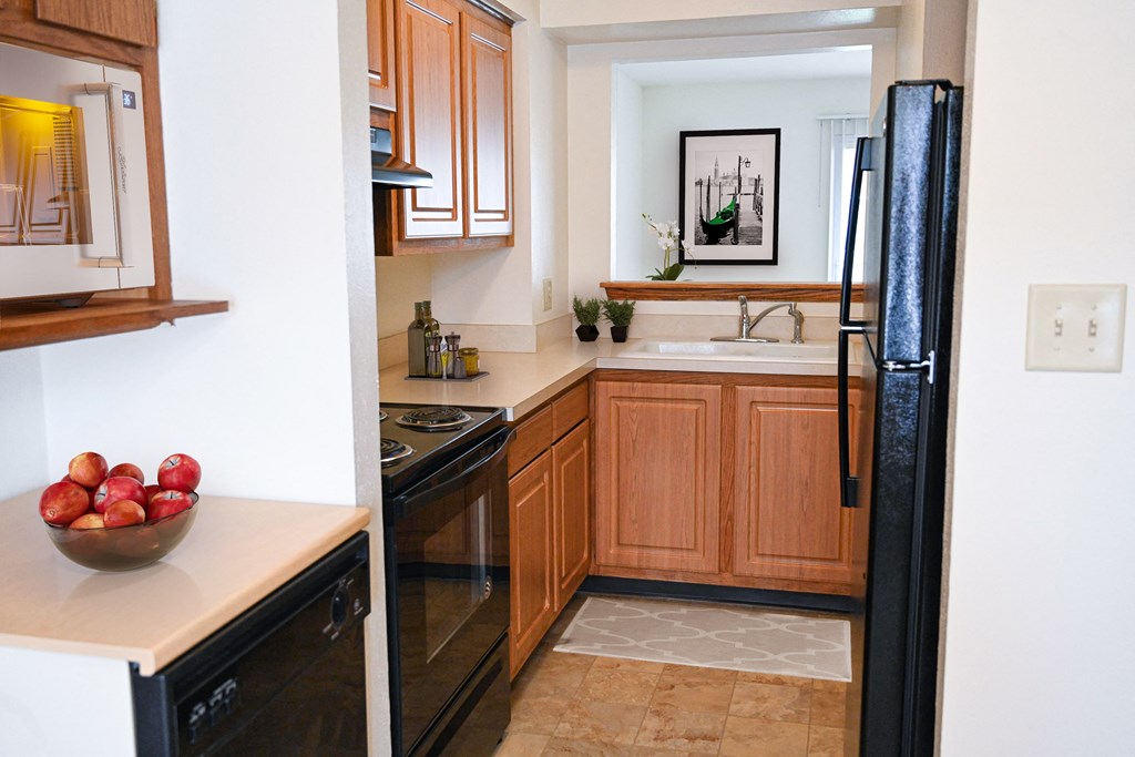 a kitchen with black appliances and wooden cabinets and a bowl of apples