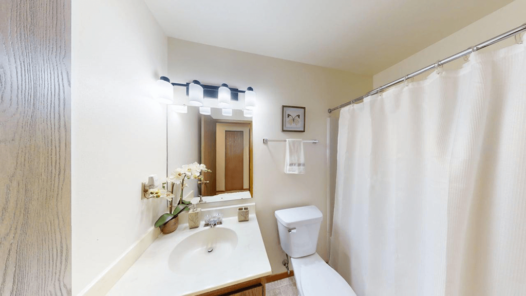 A white bathroom with a sink, mirror, toilet and shower curtain.
