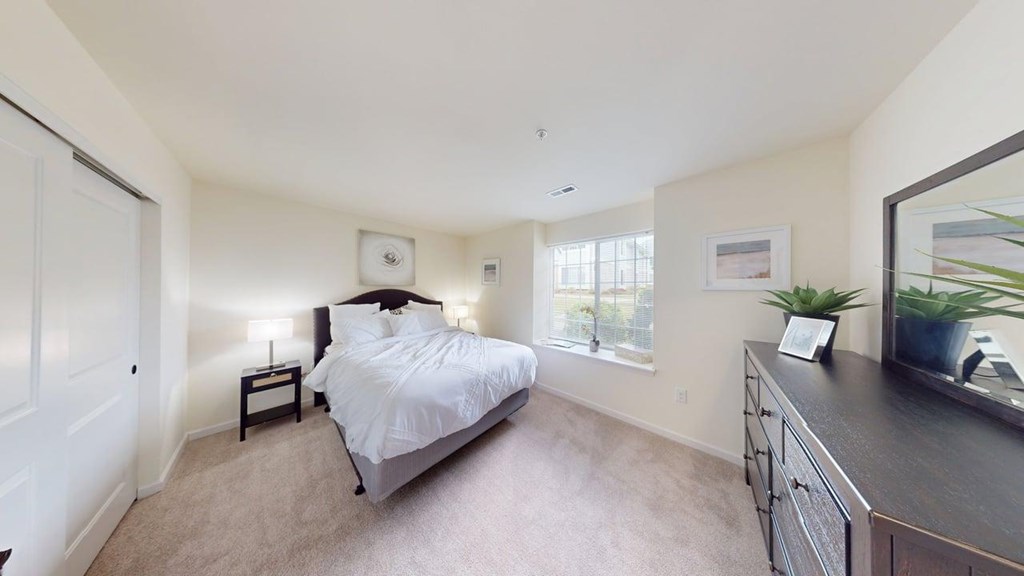 A bedroom with a bed, nightstand, and a plant on the dresser.