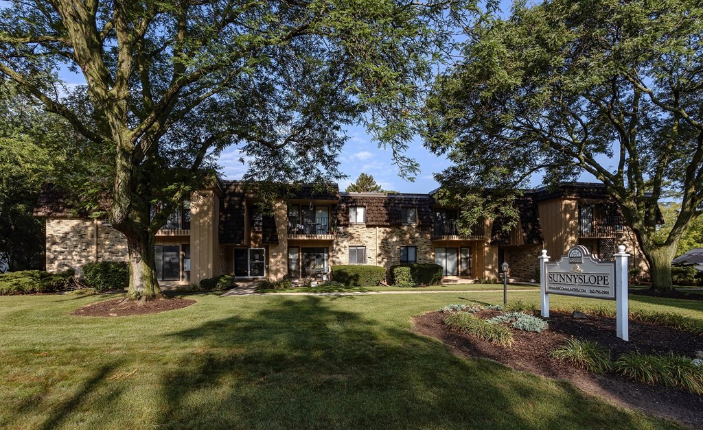 a mansion with a sign in front of a lawn and trees