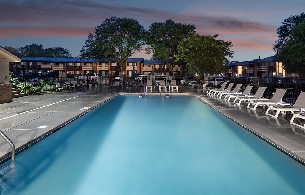 a swimming pool at night with chairs around it