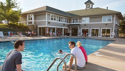 a group of people sitting at a pool with a building in the background