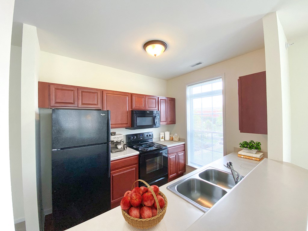 full kitchen with black appliances and white countertops with a basket of fruit