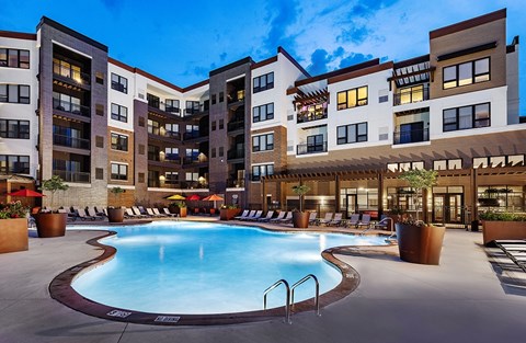 A large swimming pool is surrounded by a patio area with chairs and umbrellas.