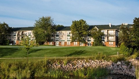 a grassy area with a pond in front of an apartment complex