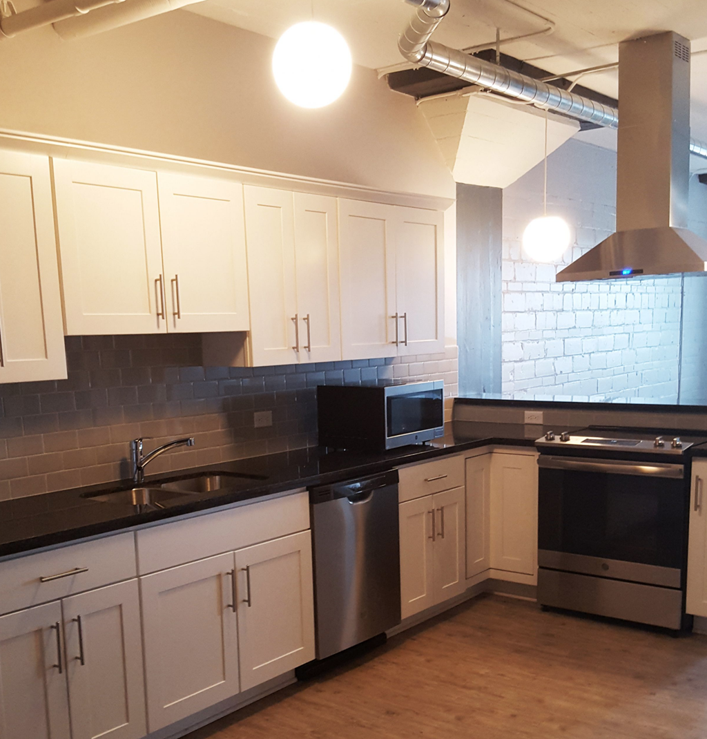 a kitchen with white cabinets and stainless steel appliances and a brick wall